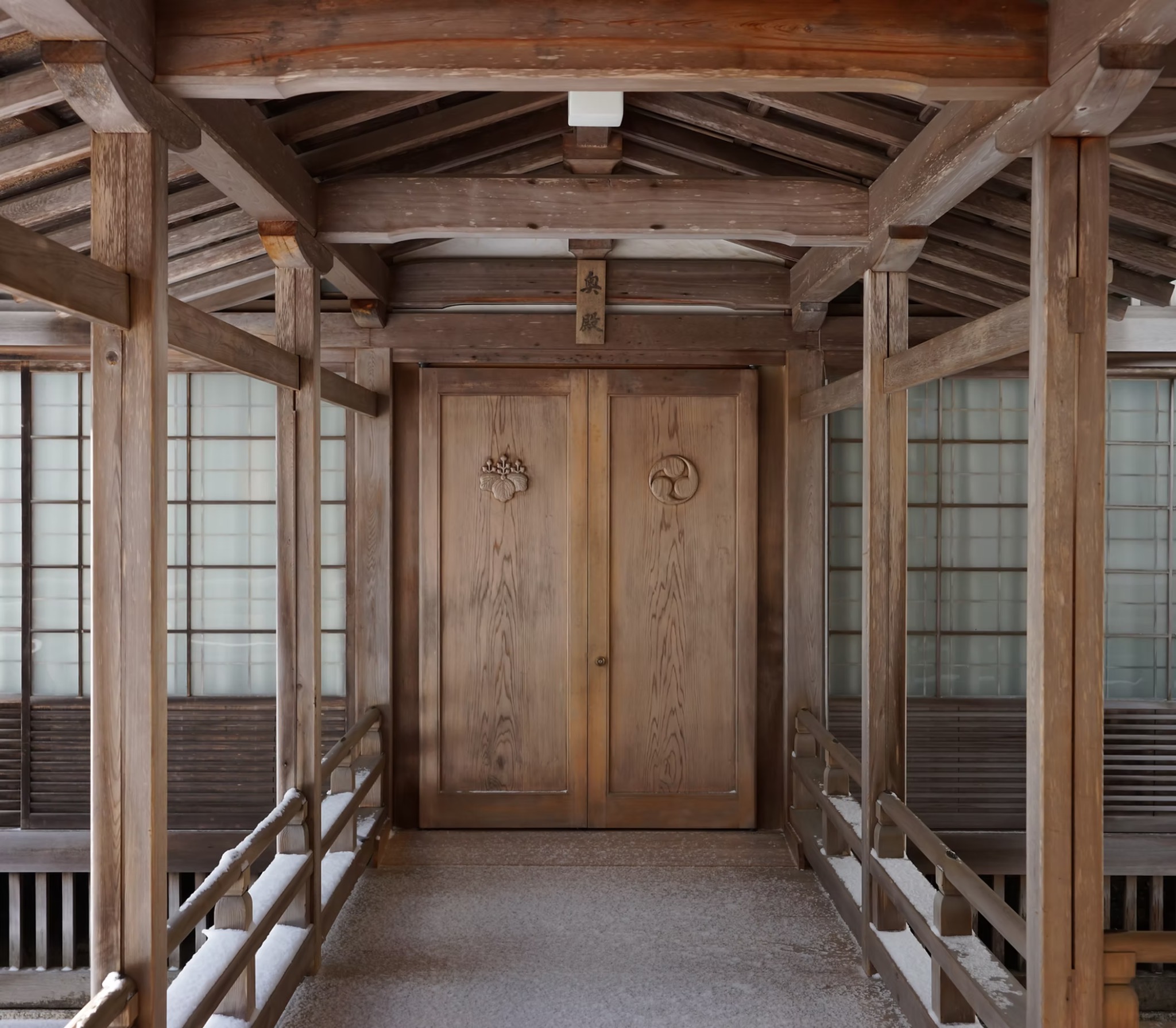 「奥殿」の扁額が掲げられた金剛峯寺の木の扉と、雪の残る渡り廊下
